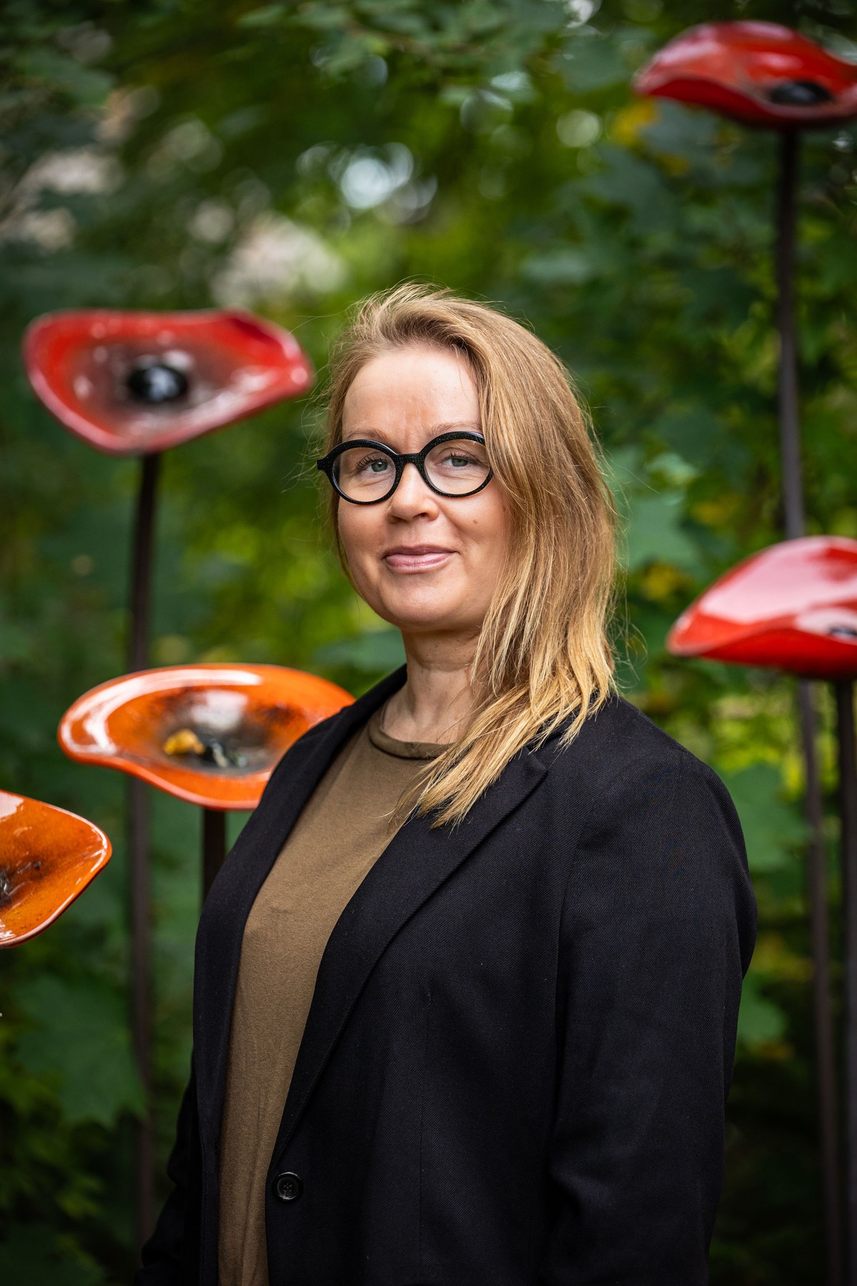 Muotokuva Merja Pennasesta ulkona punaisten taideteosten keskellä.